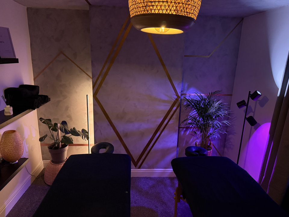 Two massage beds beneath warm woven lighting with geometric gold wall details