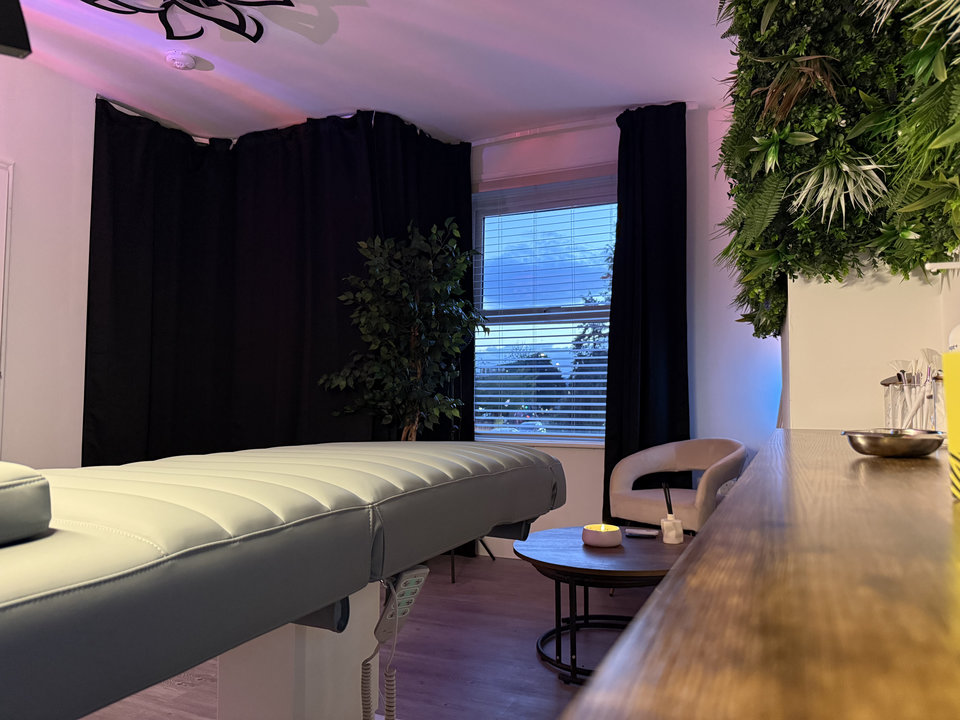 Treatment bed, dark curtains and a chair beside the studio window, with greenery above